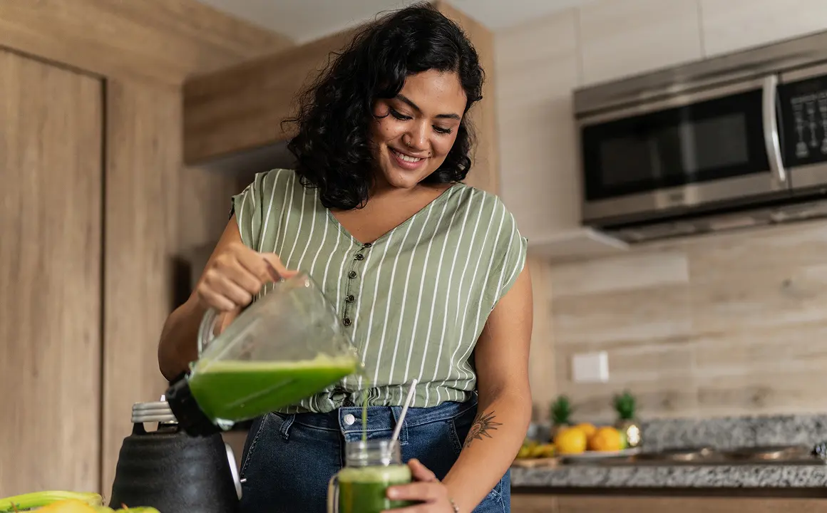 Woman pouring green smoothie in kitchen